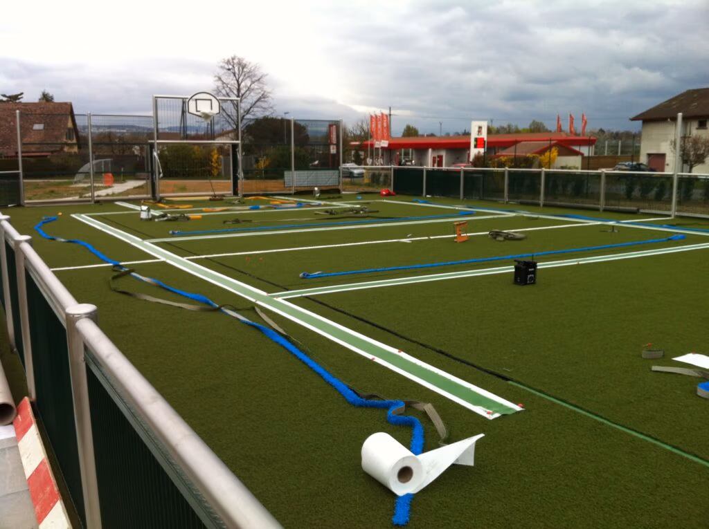 Pose du tapis synthétique sur un mini-stade à Echandens.